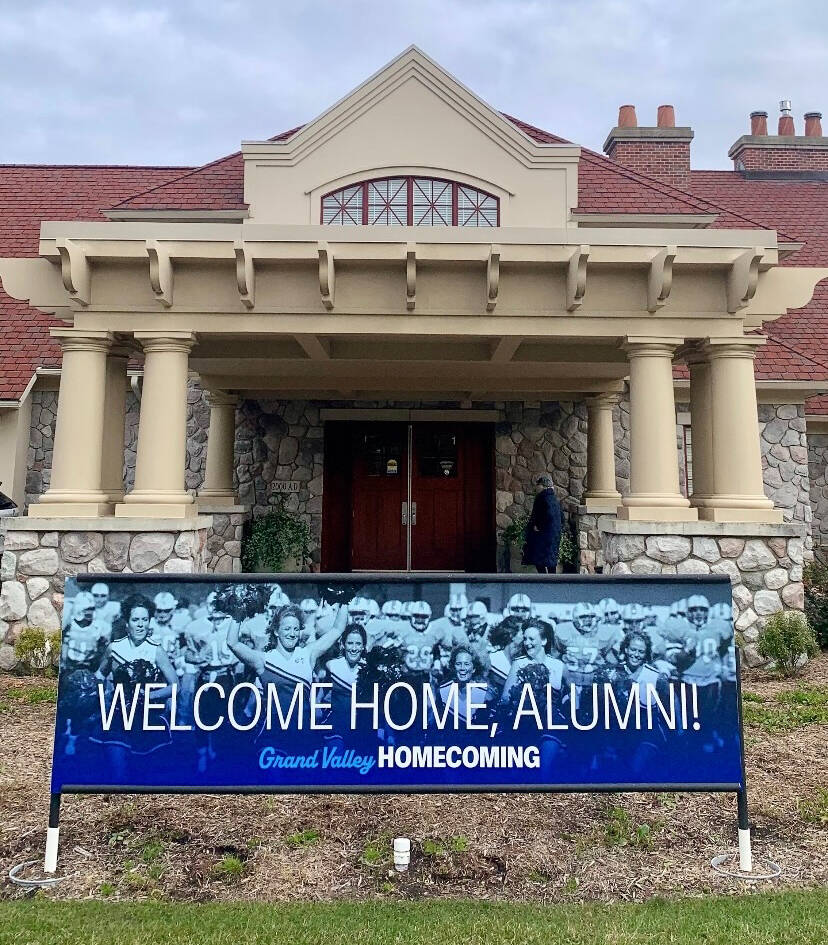 Alumni House exterior with banner, Welcome Home, Alumni, Grand Valley Homecoming on lawn in front.